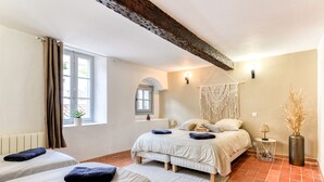A bedroom with two beds, a window with curtains, a bedside table with a lamp, and a wall-mounted light fixture.