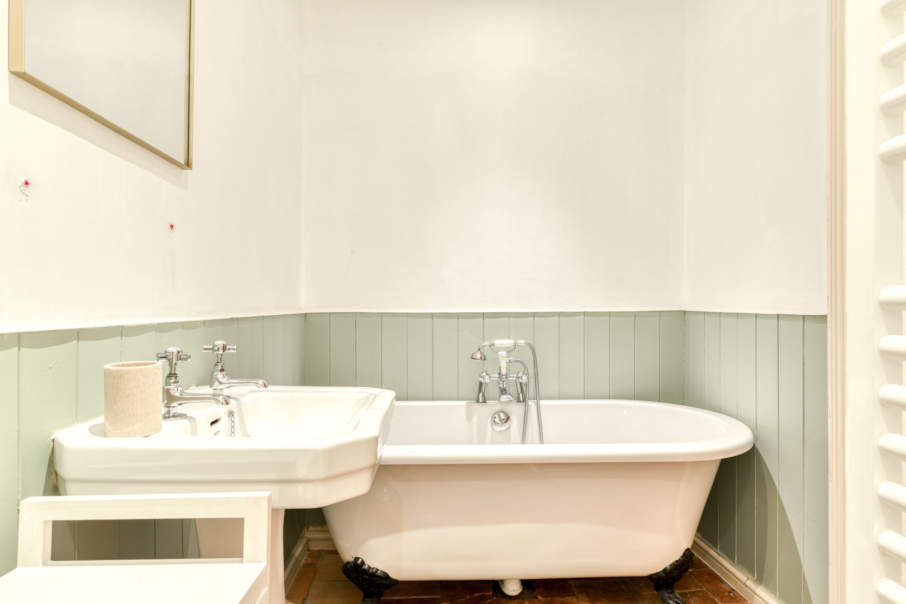 A bathroom with a white sink, a bathtub, and a mirror on the wall.