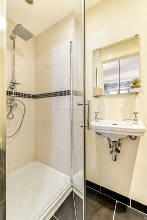 Ein Badezimmer mit Duschkabine aus Glas, einem Waschbecken mit Spiegel und einer kleinen Ablage für Toilettenartikel.
