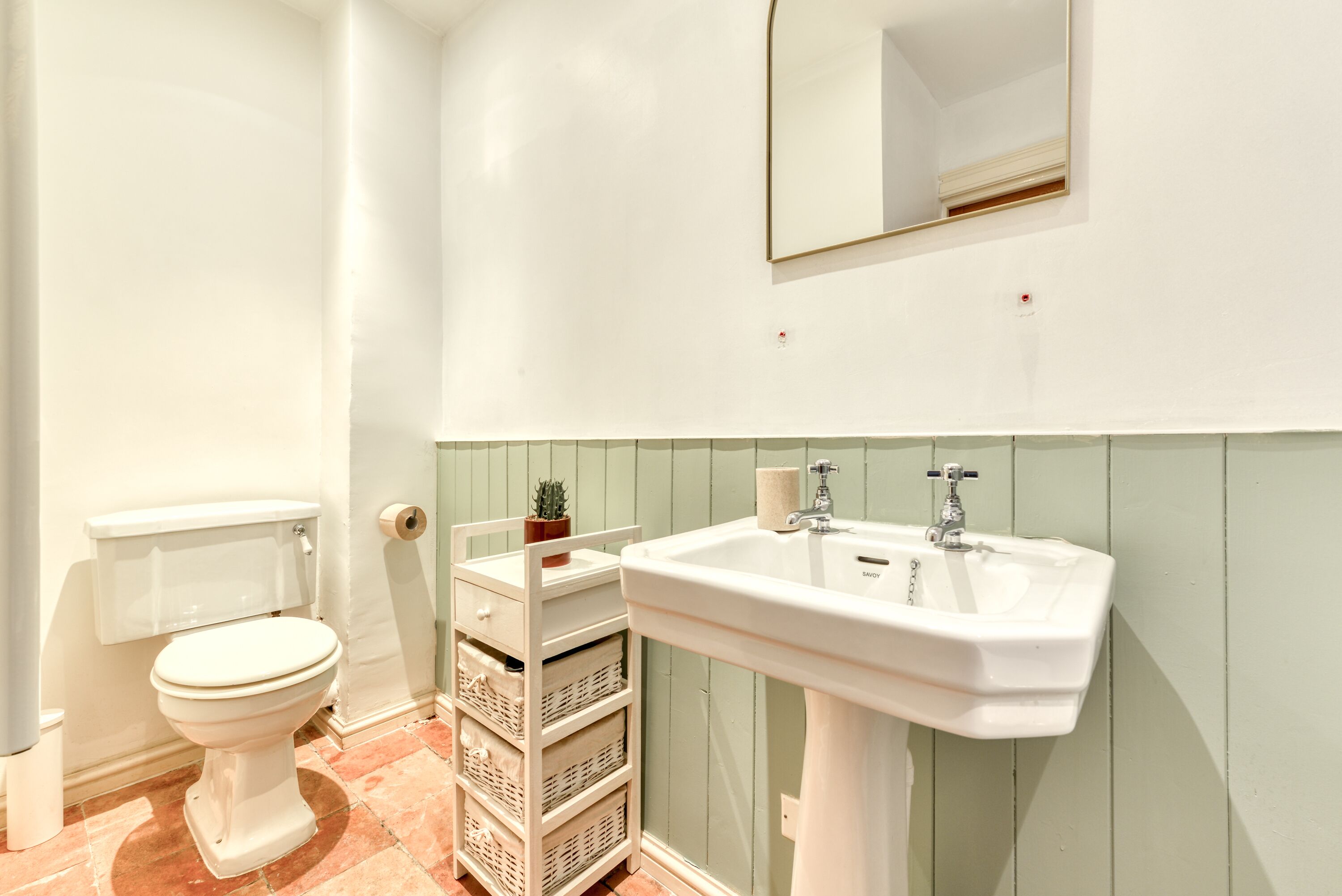 A bathroom with a toilet, a sink, a mirror, and a storage unit with baskets.