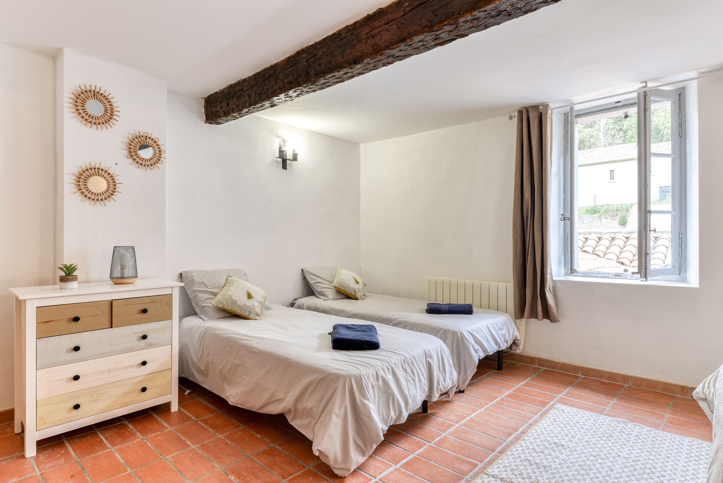 A bedroom with two beds, a dresser, and a window with curtains.
