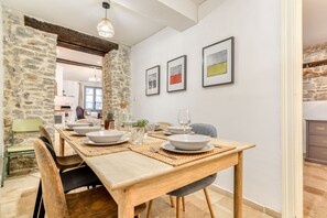 Ein Essbereich mit einem Holztisch, gedeckt für vier Personen, Steinwänden und gerahmten Bildern an der Wand.