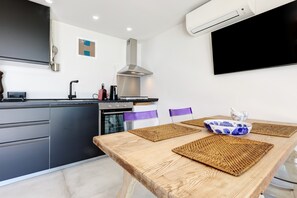 Une cuisine moderne avec une table à manger en bois, des appareils électroménagers intégrés et un téléviseur fixé au mur.