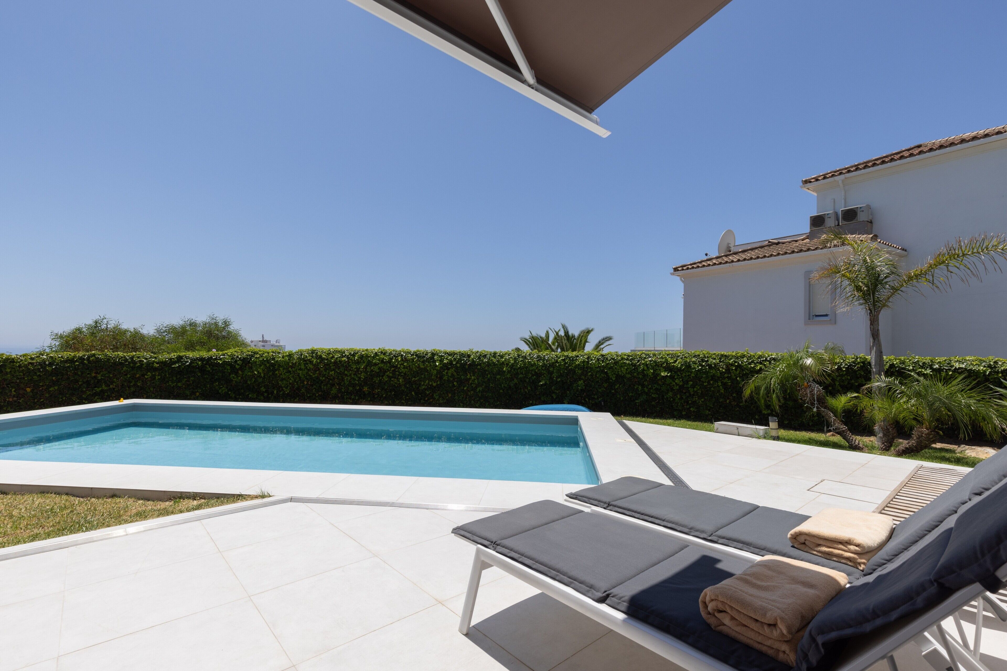 Una piscina con sillones de descanso y un edificio blanco al fondo.