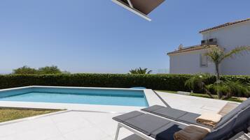 Una piscina con sillones de descanso y un edificio blanco al fondo.