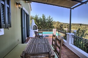 Et træbord og stole på en balkon med udsigt over et pool og træer.