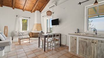 A spacious living area with a wooden ceiling, a dining table with chairs, a sofa, and a television mounted on the wall.