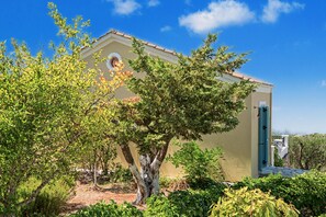 A building with a beige facade, a circular window, and a tree in the foreground. - Holiday Home 'Villa Ostria' with Sea View, Private Pool and Wi-Fi (Tsoukalades)