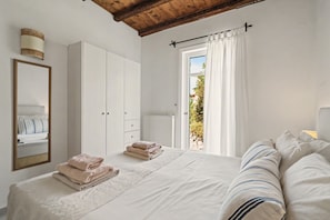 A bedroom with a bed, a wardrobe, a mirror, and a window with curtains.