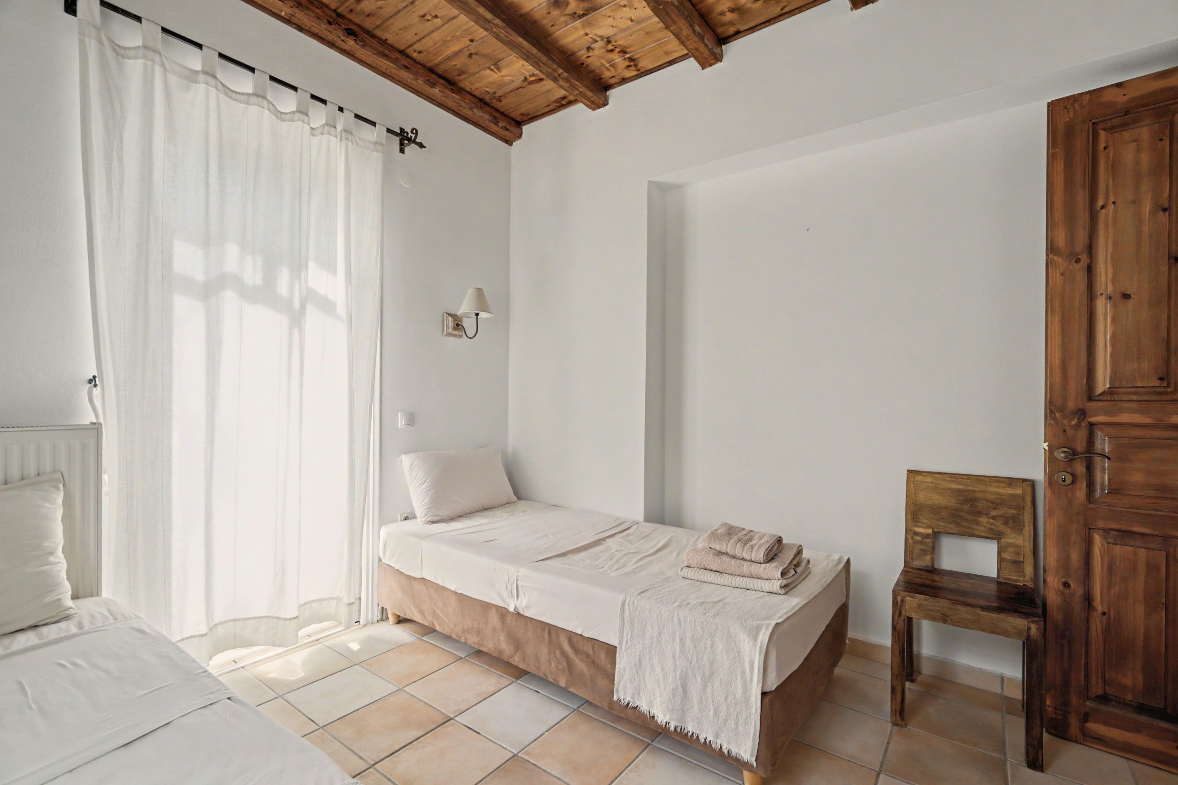 Een slaapkamer met een enkel bed, een houten stoel, een houten deur en een witte radiator.