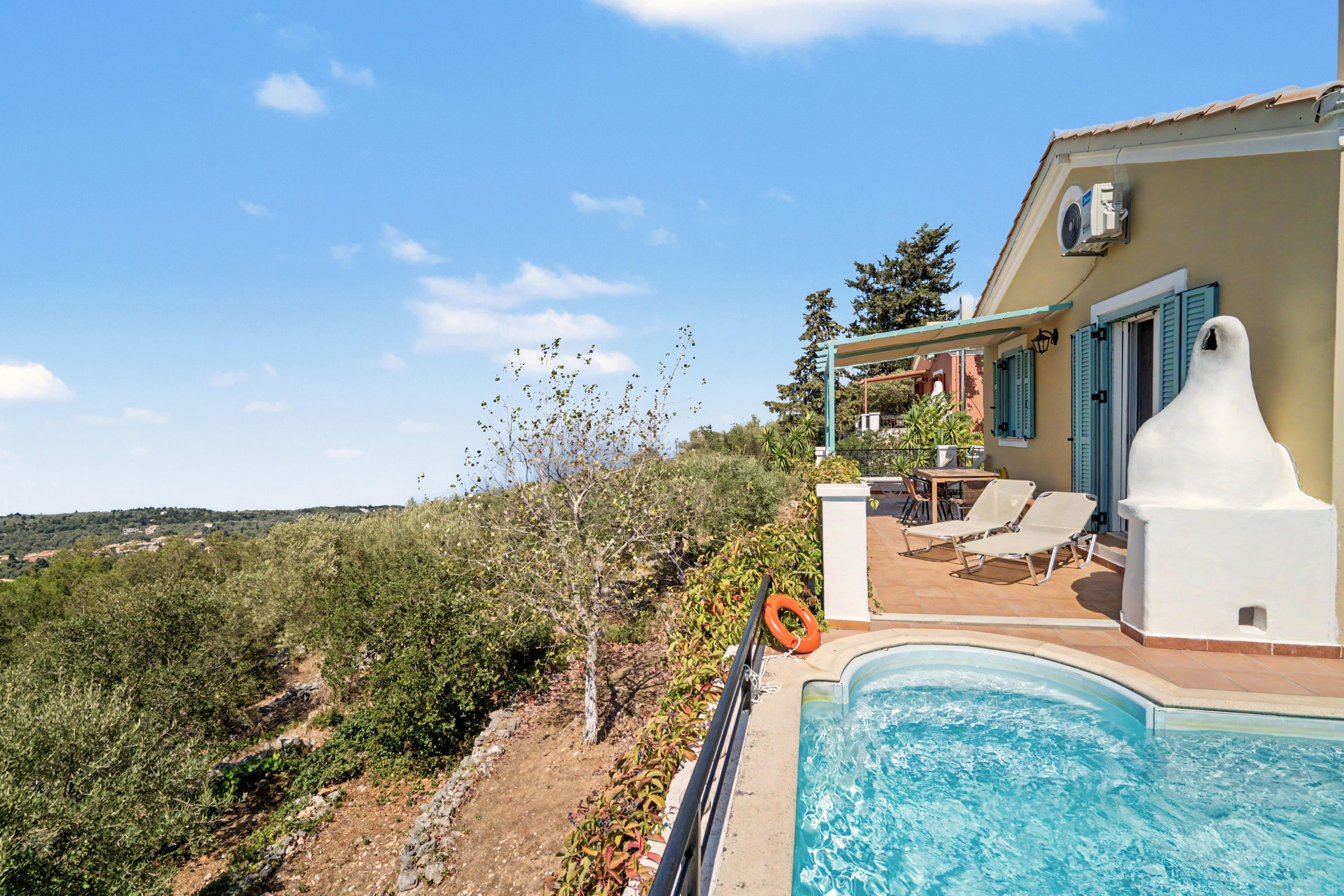 Un espace aménagé au bord de la piscine, avec vue sur une colline, un coin salon abrité et une bouée de sauvetage.