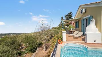 Un espace aménagé au bord de la piscine, avec vue sur une colline, un coin salon abrité et une bouée de sauvetage.