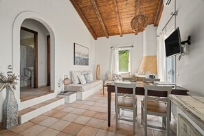 Een ruime woonkamer met hoog houten plafond, een eettafel en een bank.