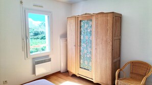 Una habitación con cama, armario, silla, radiador y ventana con vista a zonas verdes.