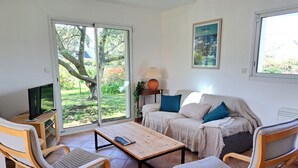 Una sala de estar con un sofá, dos sillones, una mesita de centro, un televisor y una puerta corrediza de vidrio que da a un jardín.