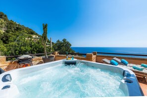 Un jacuzzi avec vue sur la mer, entouré de chaises longues et d’un espace patio.