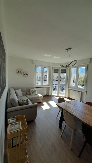 A modern living room with a sofa, a dining table, and a view through large windows.