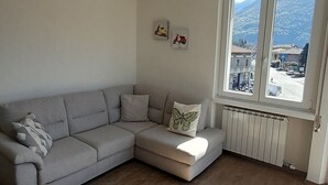 Un salón con un sofá gris, una silla, un radiador y una ventana con vistas a edificios y montañas.