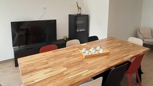 Un comedor moderno con una mesa de madera, sillas blancas y rojas, un armario negro y un televisor.