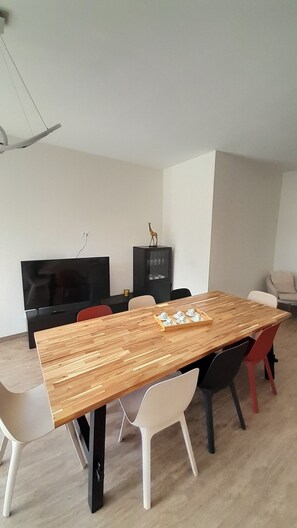 A modern dining area with a wooden table, white and red chairs, a black cabinet, and a television.