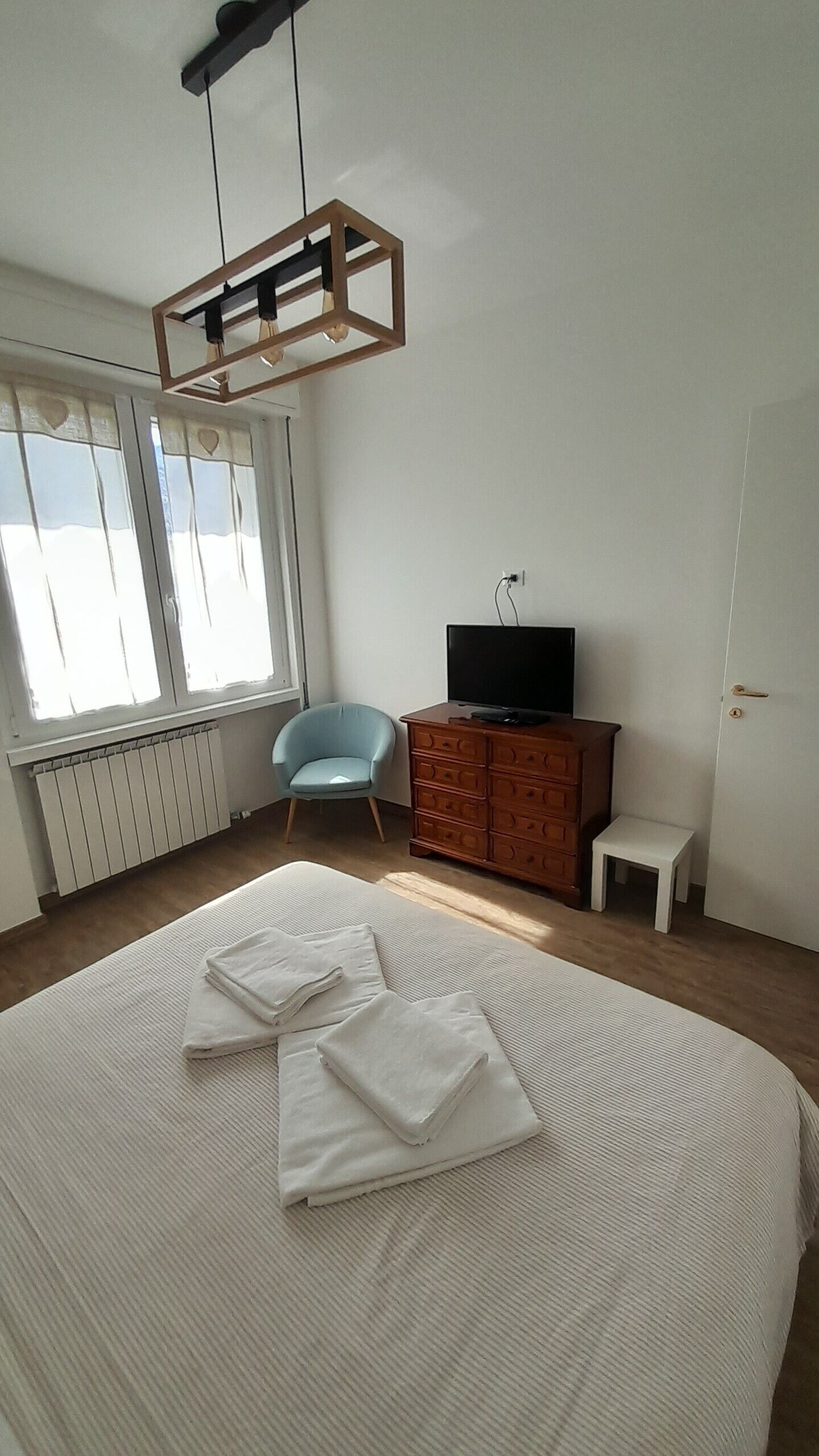 Un dormitorio con una cama, una silla, un tocador, un televisor y un radiador.