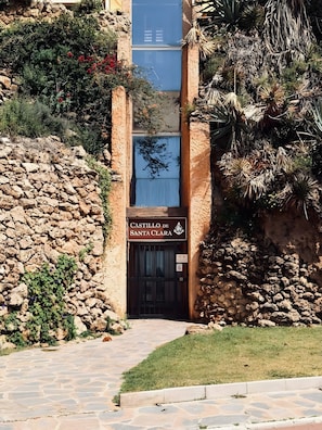 A stone building with a sign reading 'CASTILLO DE SANTA CLARA' and a gated entrance.