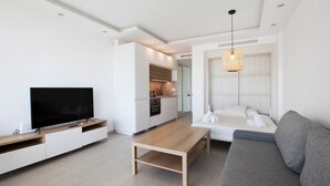 A modern living room with a flat-screen TV, wooden coffee table, grey sofa, and a kitchen in the background. - Studio Apartment 'Casa Pedro Santa Clara' with Sea View, Pool, and Wi-Fi (Torremolinos)