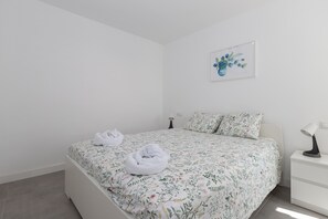 Un lit bien fait, avec une literie à motifs floraux, une table de chevet avec une lampe et une œuvre d’art florale encadrée accrochée au mur.