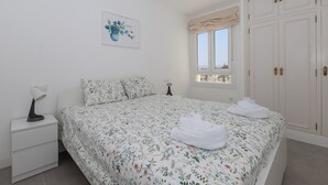 Une chambre à coucher avec une couvre-lit à motifs floraux, une lampe de chevet, une table de nuit, une fenêtre donnant sur un beau paysage et une armoire.
