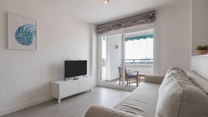 Un salon moderne doté d’un téléviseur à écran plat, d’un canapé, d’une table à manger avec des chaises et d’un balcon offrant une vue agréable.