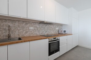 Une cuisine avec des armoires blanches, un plan de travail en bois, un four encastré et un four à micro-ondes.