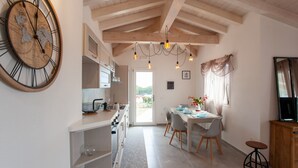 Una cocina con un reloj de pared grande, vigas de madera y un comedor con mesa y sillas.