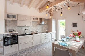 Une cuisine moderne avec des meubles blancs, un four, un évier et des luminaires suspendus.