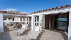 Un patio con dos tumbonas, una mesa con sillas y un ventanal de vidrio que da a una zona cubierta.