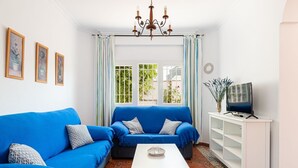 Een woonkamer met een blauwe bank, een witte salontafel en een televisie op een witte dressoir.