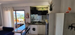 Une cuisine compacte équipée d’un lave-linge, un coin repas avec une table et des chaises, et une vue à travers une porte vitrée.