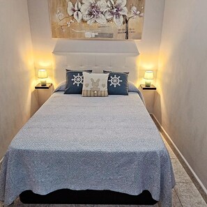 Une chambre à coucher avec un lit, deux lampes de chevet, une œuvre d’art accrochée au mur et une couvre-lit à motifs.