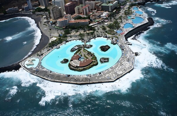 Vue aérienne d’une station balnéaire dotée de plusieurs piscines, d’un parc central et entourée d’immeubles de grande hauteur.