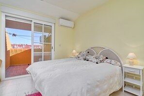 Un dormitorio con cama, mesita de noche, lámpara, aire acondicionado y una puerta corrediza de vidrio que da a un balcón.