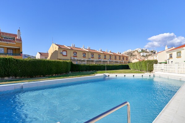 A swimming pool with a metal railing, surrounded by buildings with red-tiled roofs and a clear blue sky. - Holiday Apartment 'Casa Venus' with Sea View, Terrace, Shared Pool & Wi-Fi (Salobrena)