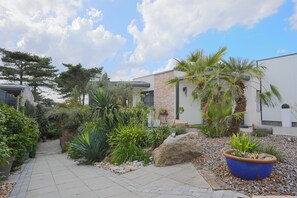 A modern building with a brick facade, surrounded by a well-maintained garden with various plants and a paved walkway. - Holiday Home 'Logement À Trebeurden 800m Plage' with Private Terrace, Wi-Fi and Air Conditioning (Trébeurden)