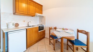 Een functionele keuken met houten kastjes, een wit aanrecht, een kleine koelkast, een magnetron en een eettafel met stoelen.