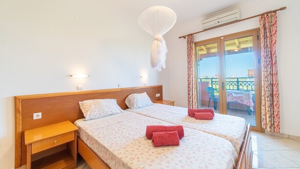 Een tweepersoonsbed met bloemenbeddengoed, een nachtkastje, een hangend klamboes en uitzicht op het balkon.