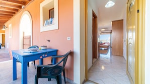 Una habitación con techo de madera, una mesa azul con sillas, una puerta con pomo dorado y suelo de baldosas.