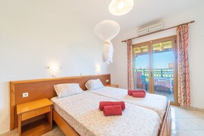 Una cama doble con ropa de cama floral, una mesita de noche, una mosquitera colgante y vistas al balcón exterior.