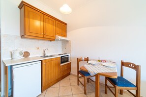 Une cuisine compacte avec des meubles en bois, un réfrigérateur blanc, un four à micro-ondes et une table à manger avec des chaises.