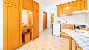 Une cuisine avec des meubles de rangement en bois, une table à manger recouverte d’une nappe à carreaux et un réfrigérateur.