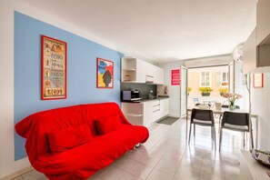 A modern living space with a red sofa, a kitchen area, and a dining table with chairs.