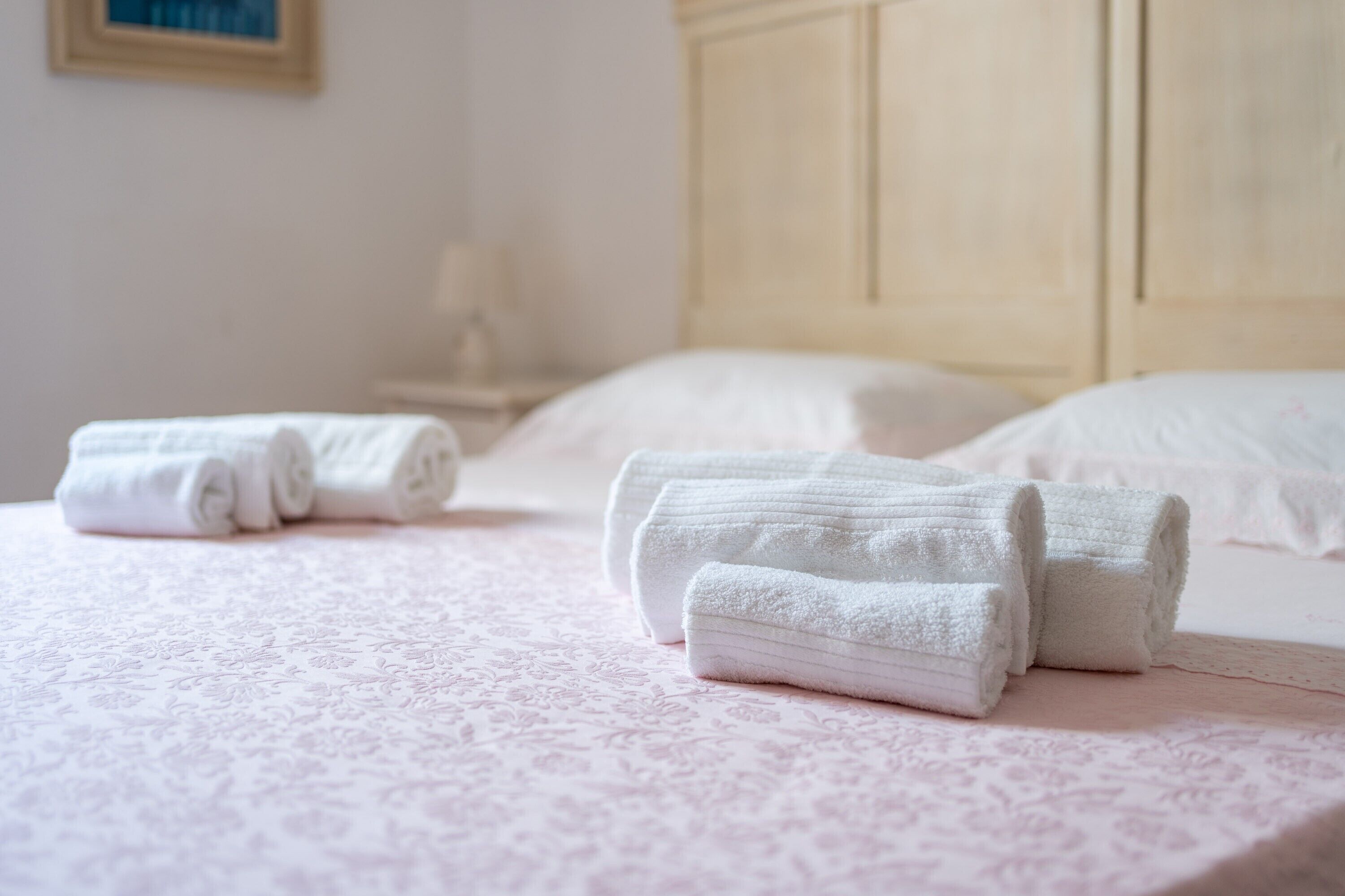 Una cama bien hecha con toallas blancas enrolladas, un cabecero de madera y una mesita de noche con una lámpara.