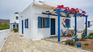 A white building with blue accents, stone flooring, and a covered outdoor seating area with potted plants.